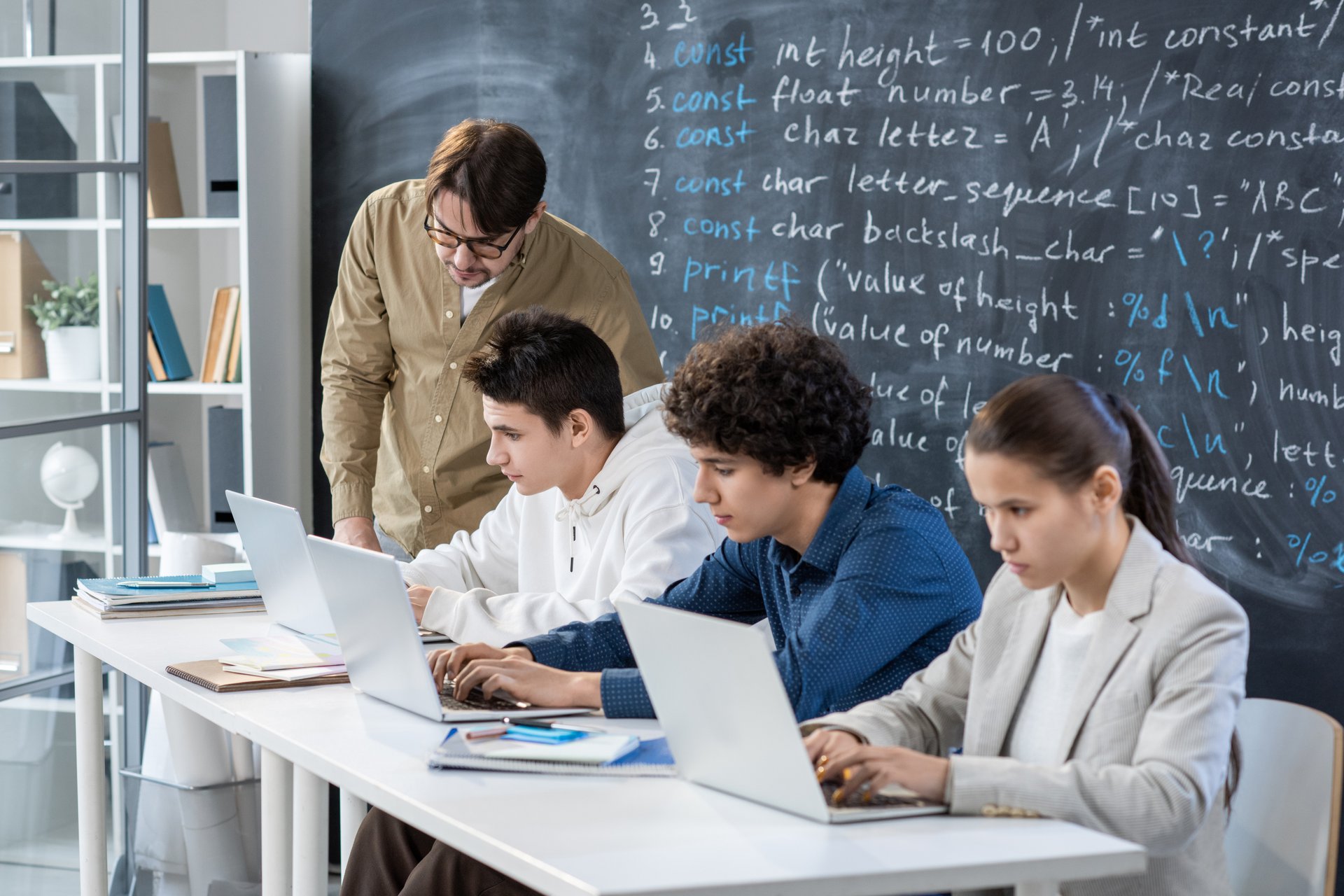A trainer checking one student's individual work at a desk, the assessor review step that signs off every drafted feedback comment