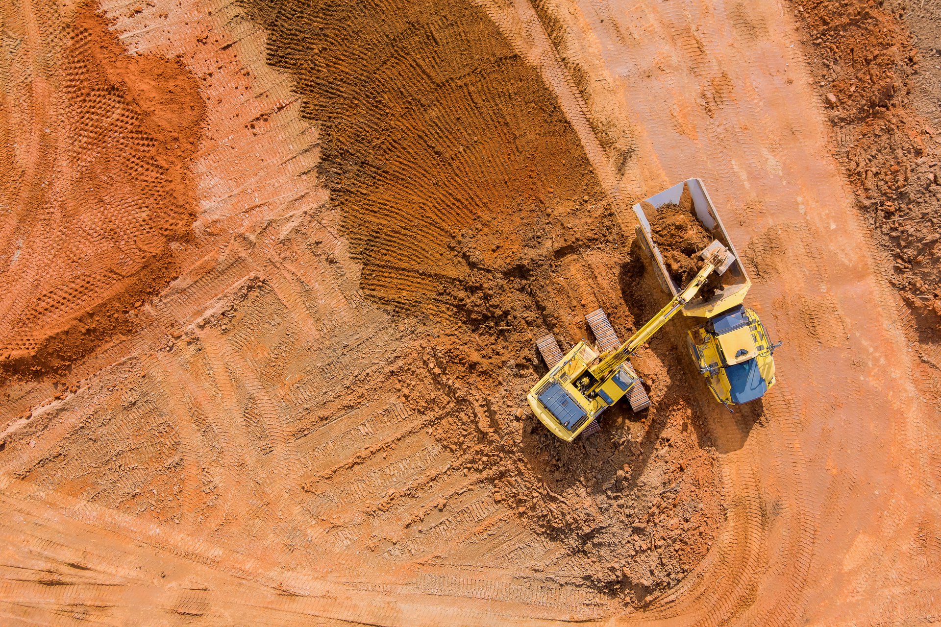 An aerial view of a bulldozer scraping a layer of earth at a mine site, the harsh remote environment the field app is built for.